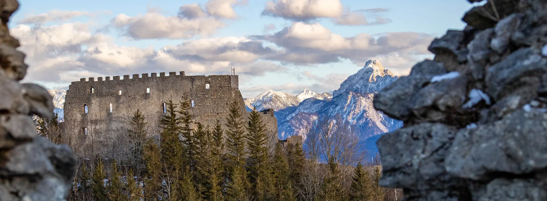 Blick auf die Burgruine Eisenberg in einer tollen Bergkulisse mit weißen Gipfeln.