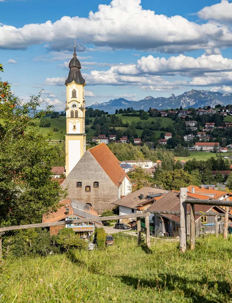 Pfronten im Allgäu entdecken Blick vom Aussichtspunkt "Hörnle" auf die Pfrontener Kirche und die dahinterliegende Berglandschaft.