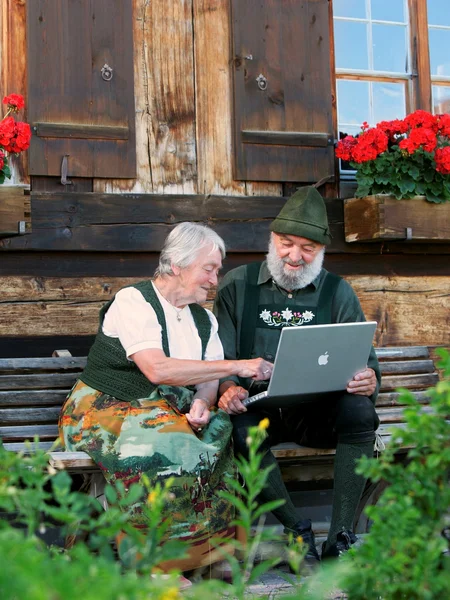 WLAN in Pfronten im Allgäu Zwei Personen in Tracht sitzen auf einer Bank und schauen auf ihren Laptop.