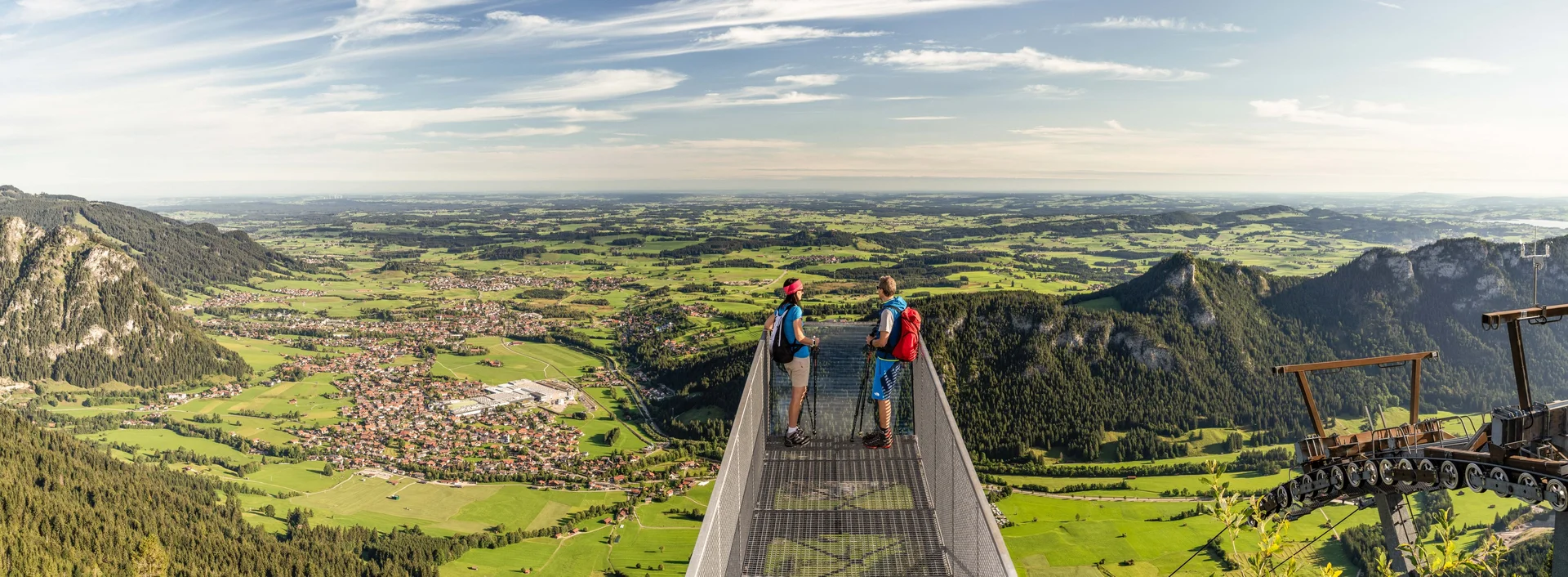 Weitreichender Blick über den Aussichtssteg auf dem Breitenberg auf das Pfrontener Tal und die umliegende Berglandschaft.