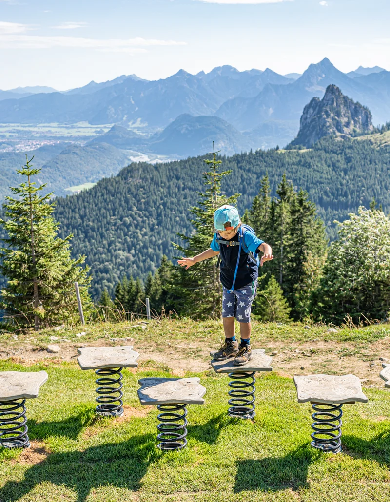 Ein Kind auf dem Juwelenweg am Pfrontener Breitenberg, ein Erlebnisweg für Familien mit Blick auf die sommerliche Bergkulisse.