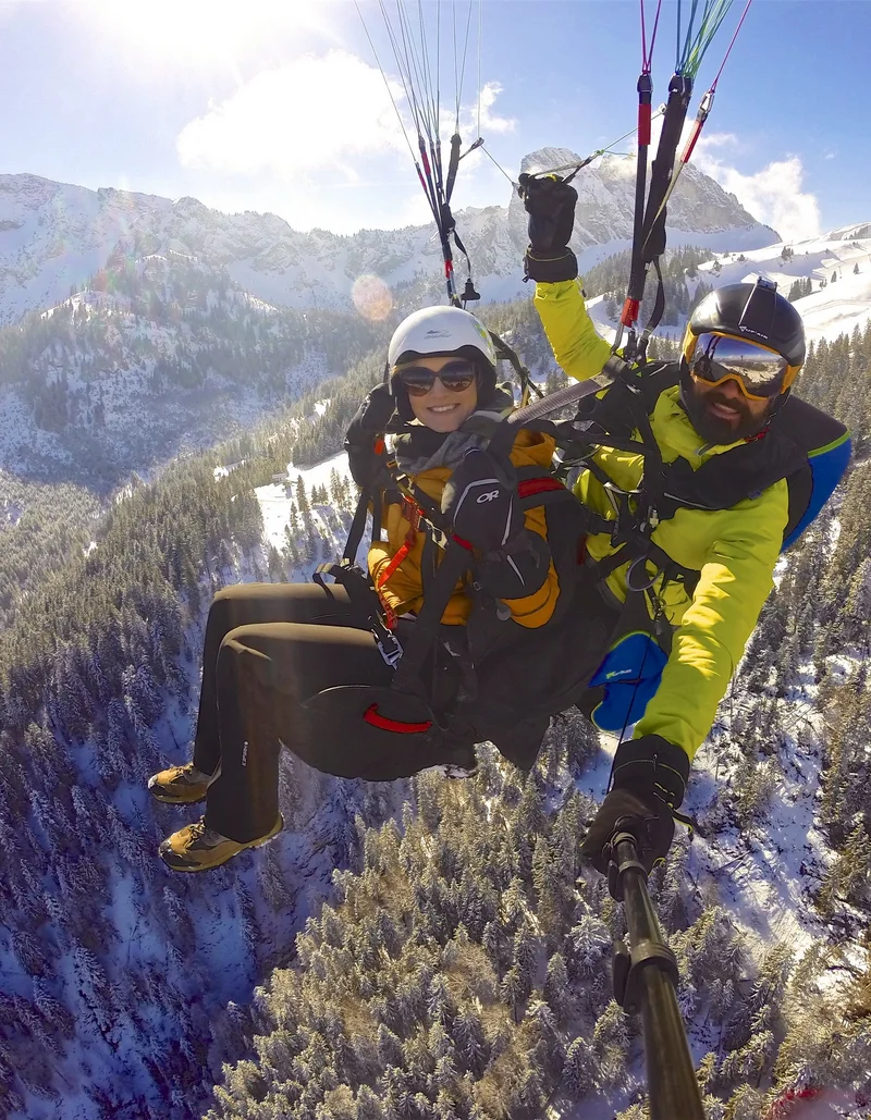 Foto von FlyRoyal Ein Tandemflug mit dem Gleitschirm bei Sonnenschein mit Blick auf eine winterliche Berglandschaft.