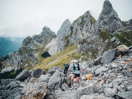 Zwei Trailrunner beim Aufstieg in einer alpinen Bergkulisse.