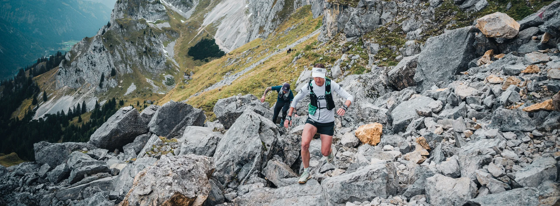 Zwei Trailrunner beim Aufstieg in einer alpinen Bergkulisse.