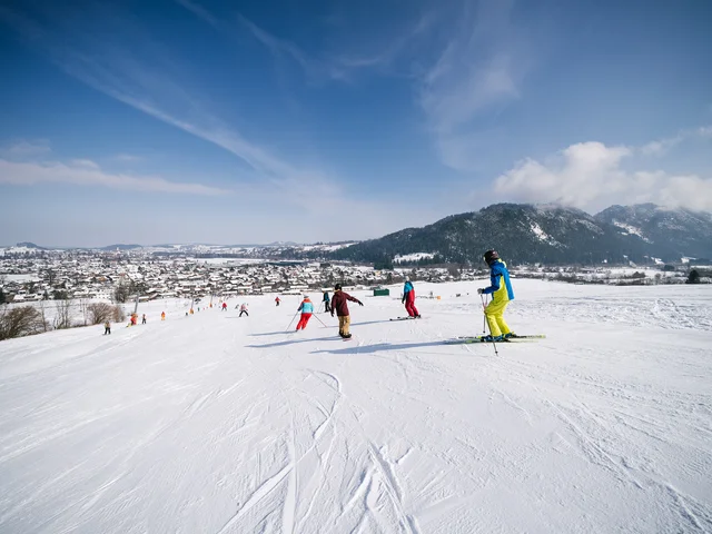Skifahrer auf der Piste, im Hintergrund ist das verschneite Tal sowie Berge zu erkennen.