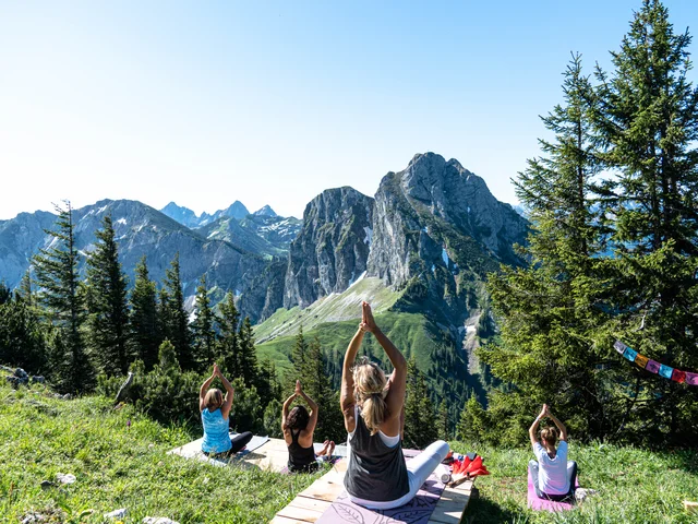 Eine Gruppe macht Yoga am Berg mit Blick auf die beeindruckende Bergkulisse.