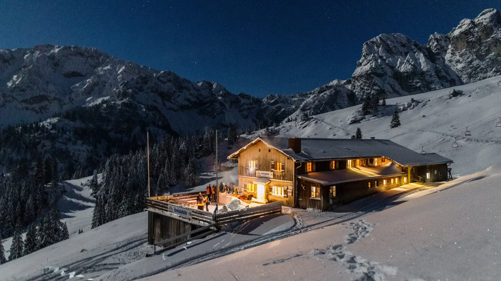 Die Hochalphütte in Pfronten in einer idyllisch verschneiten Landschaft und magischen Beleuchtungen bei Nacht. 