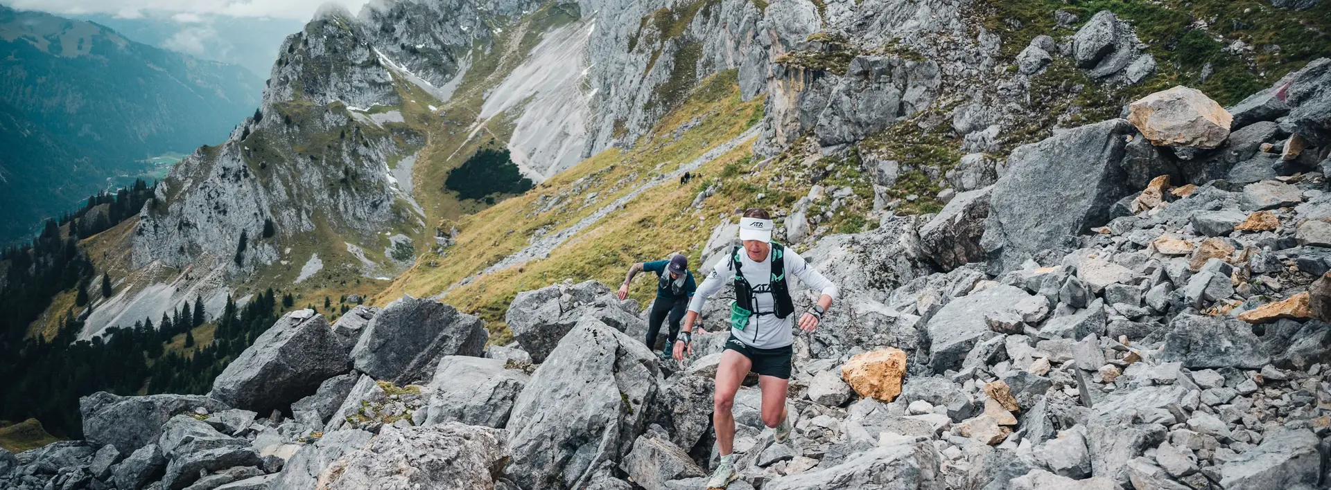 Zwei Trailrunner beim Aufstieg in einer alpinen Bergkulisse.