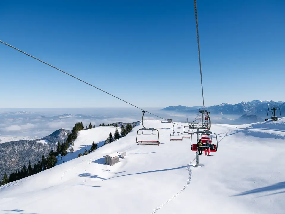 Blick von der Sesselbahn am Breitenberg über eine idyllisch verschneite Winterlandschaft mit den Allgäuer Bergen im Hintergrund.