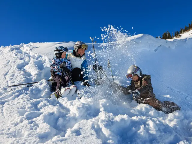 Eine Skifahrerfamilie sitzt bei sonnigem Wetter im Schnee und hat Spaß.