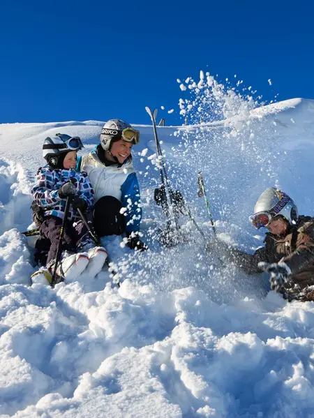 Eine Skifahrerfamilie sitzt bei sonnigem Wetter im Schnee und hat Spaß.