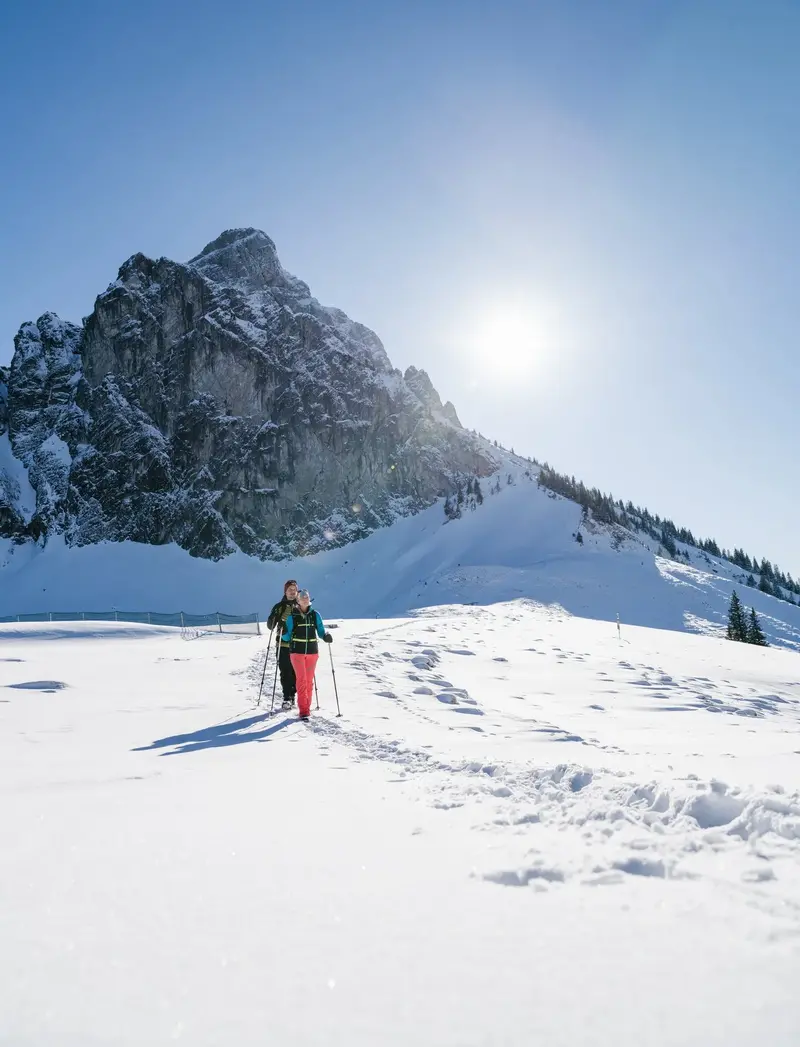 Wanderer auf verschneiten Wegen mit einem winterlichen Bergpanorama.