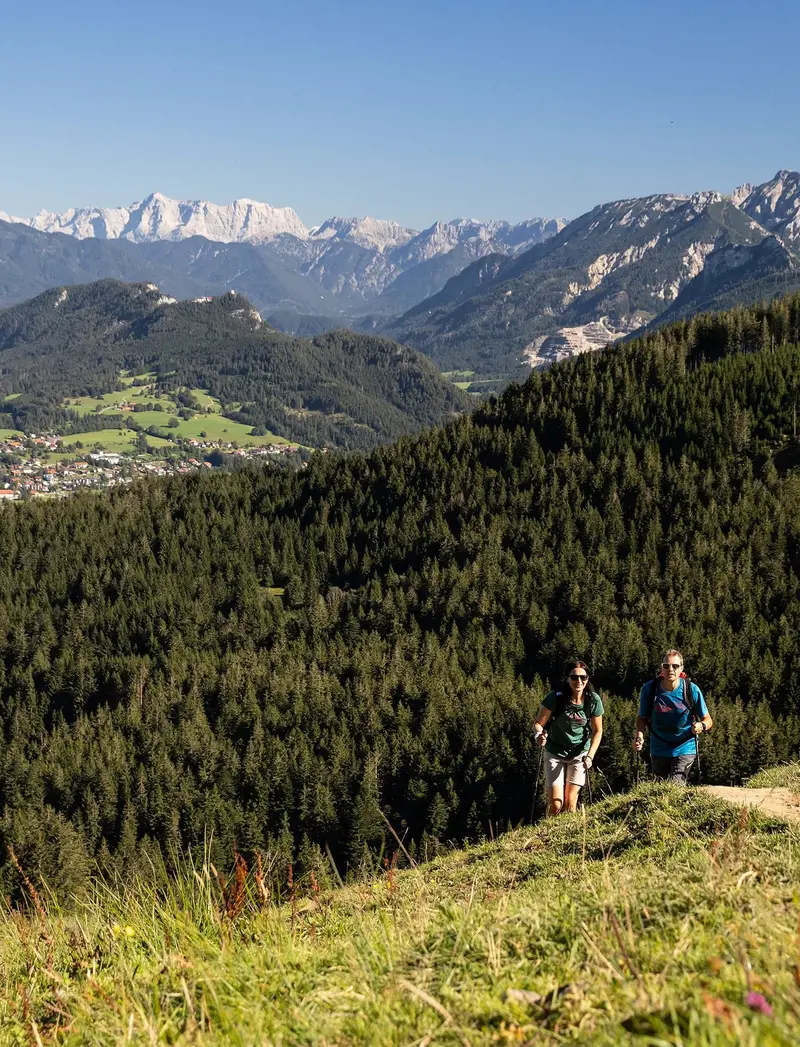 Wanderungen & Bergtouren Zwei Wanderer auf einem schmalen Pfad auf dem Berg inmitten grüner Wiesen und einer beeindruckenden Bergkulisse.